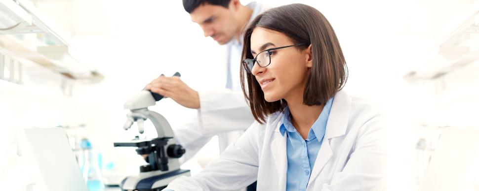 Laboratory researchers working with a microscope and a laptop.