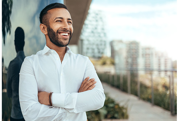Person in white shirt smiling with arms crossed outdoors.