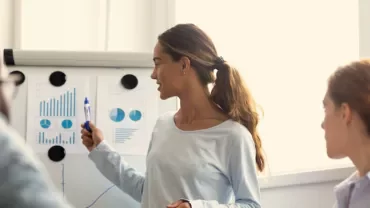 Person presenting graphs and charts to a group in a conference room.