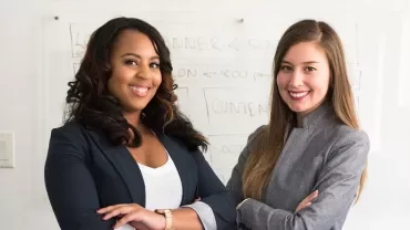 Two people smiling in a professional setting with a whiteboard in the background.