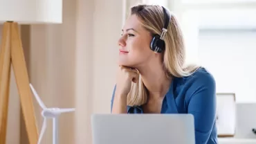 Person with headphones working at a desk with a laptop and wind turbine model.