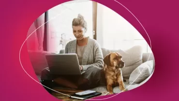 Person working on a laptop at home with a dog sitting nearby.