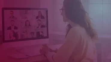 Person participating in a virtual meeting with a group of people displayed on a monitor.