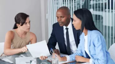 A group of colleagues talking and pointing at a report in an office