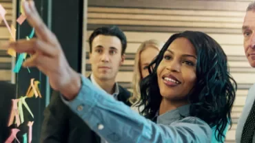 a woman pointing to a post it next to a group of people
