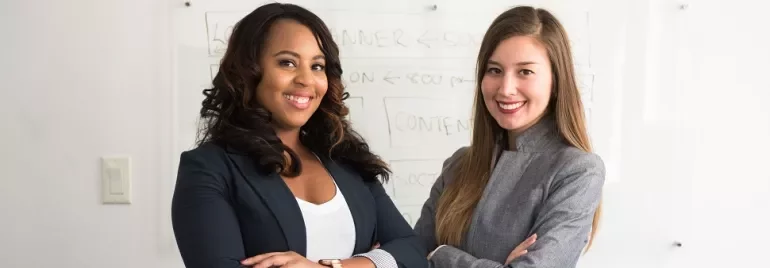 Two people smiling in a professional setting with a whiteboard in the background.