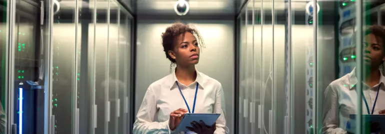 Person in a server room holding a tablet, looking at equipment.