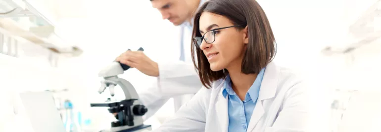 Laboratory researchers working with a microscope and a laptop.