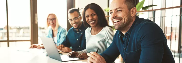 Group of people smiling and sitting at a conference table.