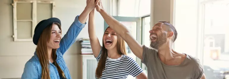 Three people smiling and giving a high five in a sunlit room.