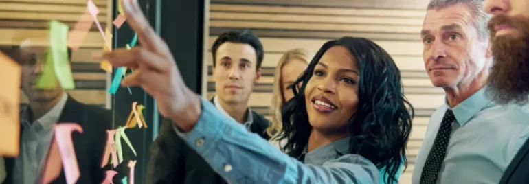 a woman pointing to a post it next to a group of people