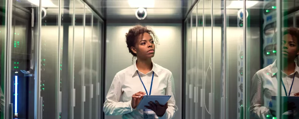 Person in a server room holding a tablet, looking at equipment.