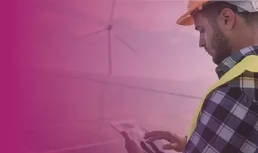 Person in safety gear using a tablet near wind turbine.