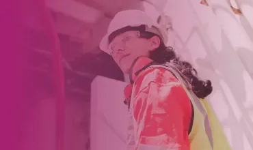 Person in safety gear standing outside, gazing to the side, with industrial background and soft pink overlay.