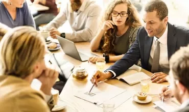 Group of people having a meeting at a table with documents and laptops.