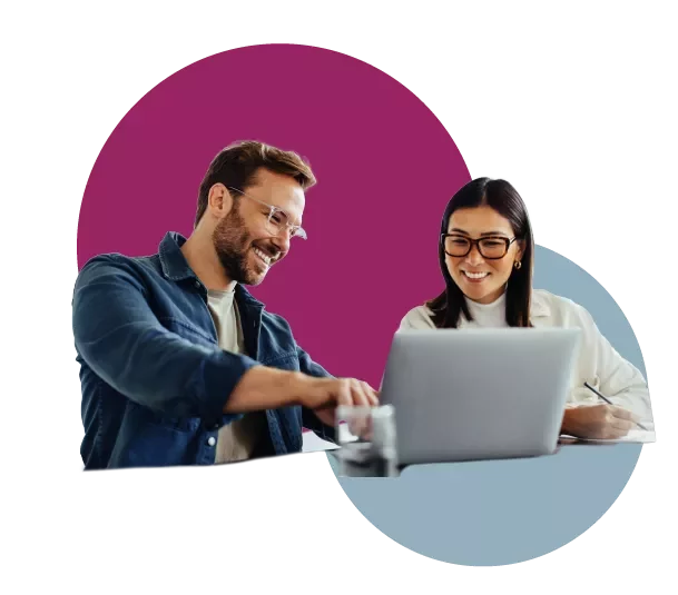 Two people smiling while working on a laptop together.